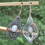 Pair of silver filigree earrings with a central gemstone on a wooden stick against a blurred green background.