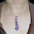 Necklace with a purple gemstone pendant on a person wearing a brown top.