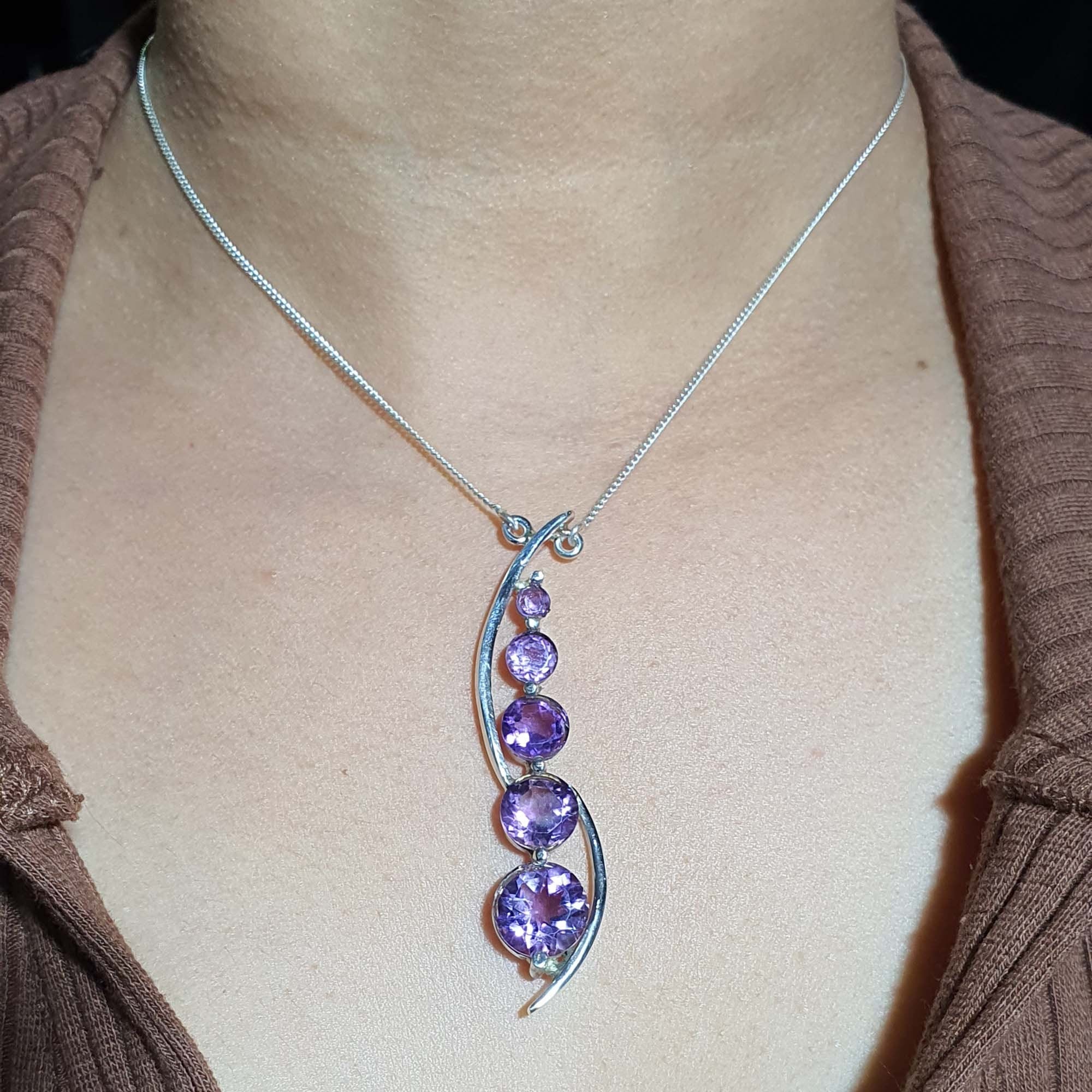 Necklace with a purple gemstone pendant on a person wearing a brown top.