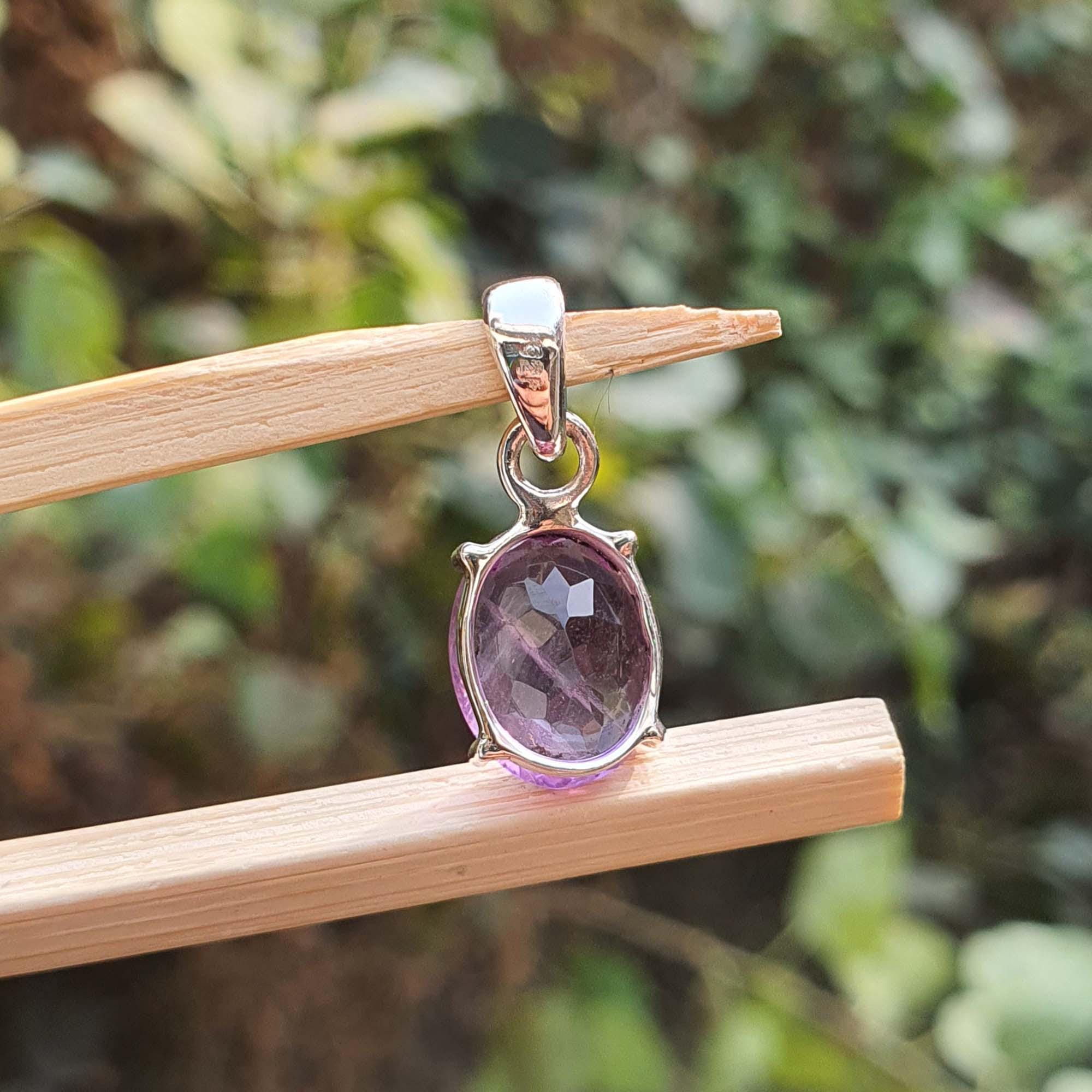 Amethyst pendant on a wooden stick with a blurred green background
