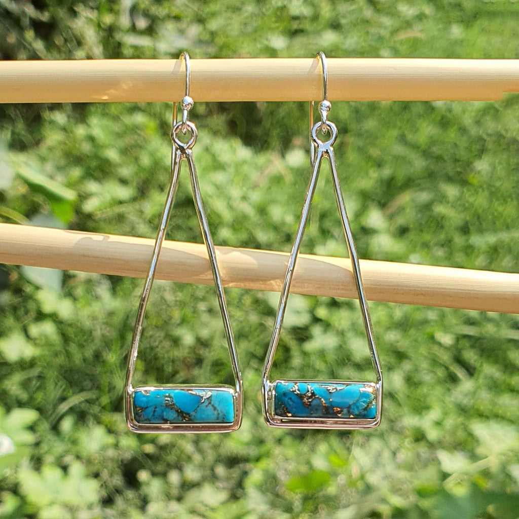 Pair of silver earrings with turquoise stones on a wooden stick against a green foliage background