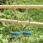 Pair of silver earrings with turquoise stones on a wooden stick against a green foliage background