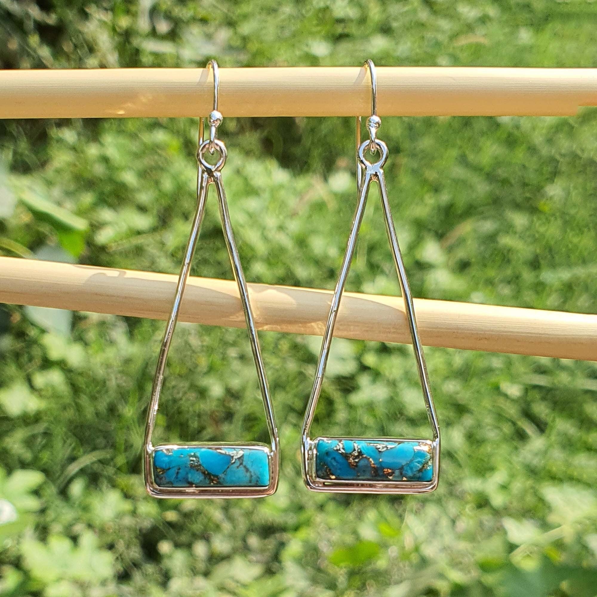 Pair of silver earrings with turquoise stones on a wooden stick against a green foliage background