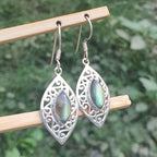 Silver earrings with gemstones on a wooden stick against a green leafy background