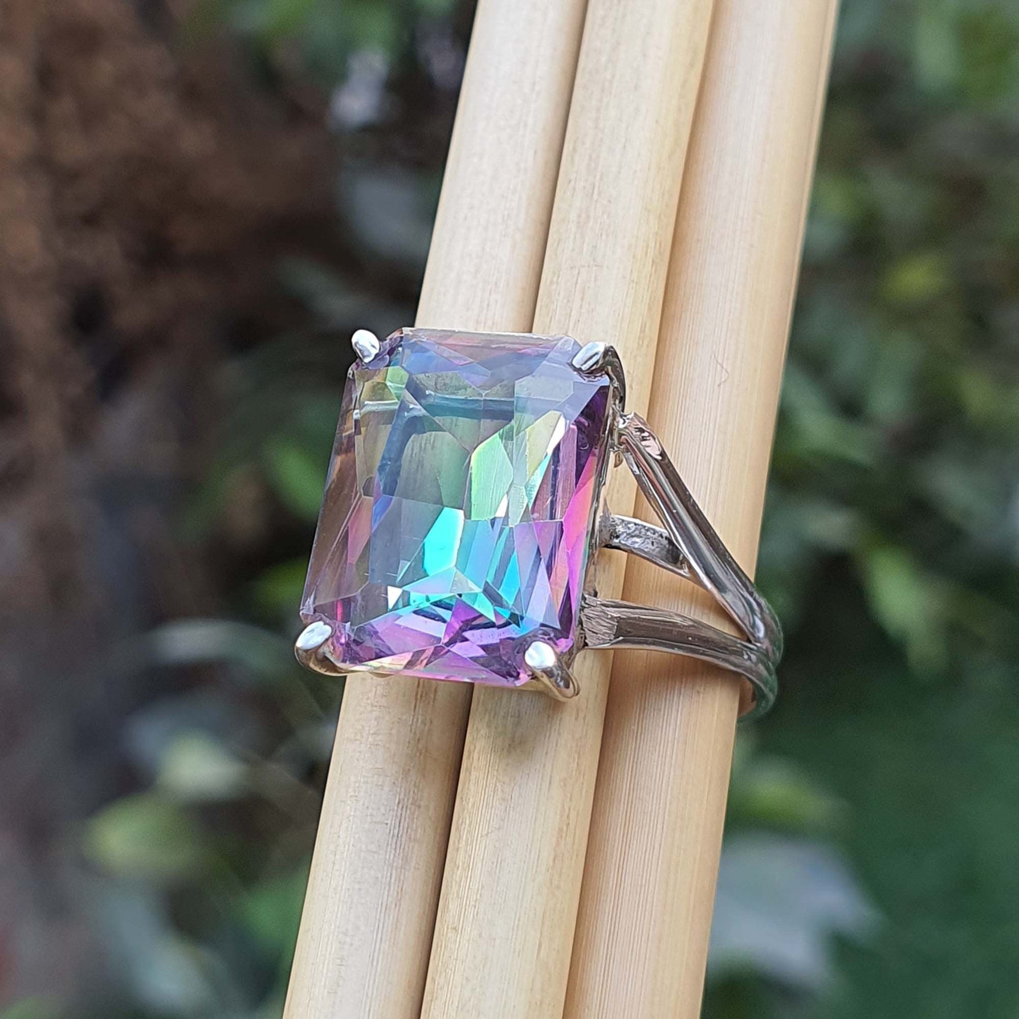Ring with a colorful gemstone held on wooden sticks against a blurred natural background