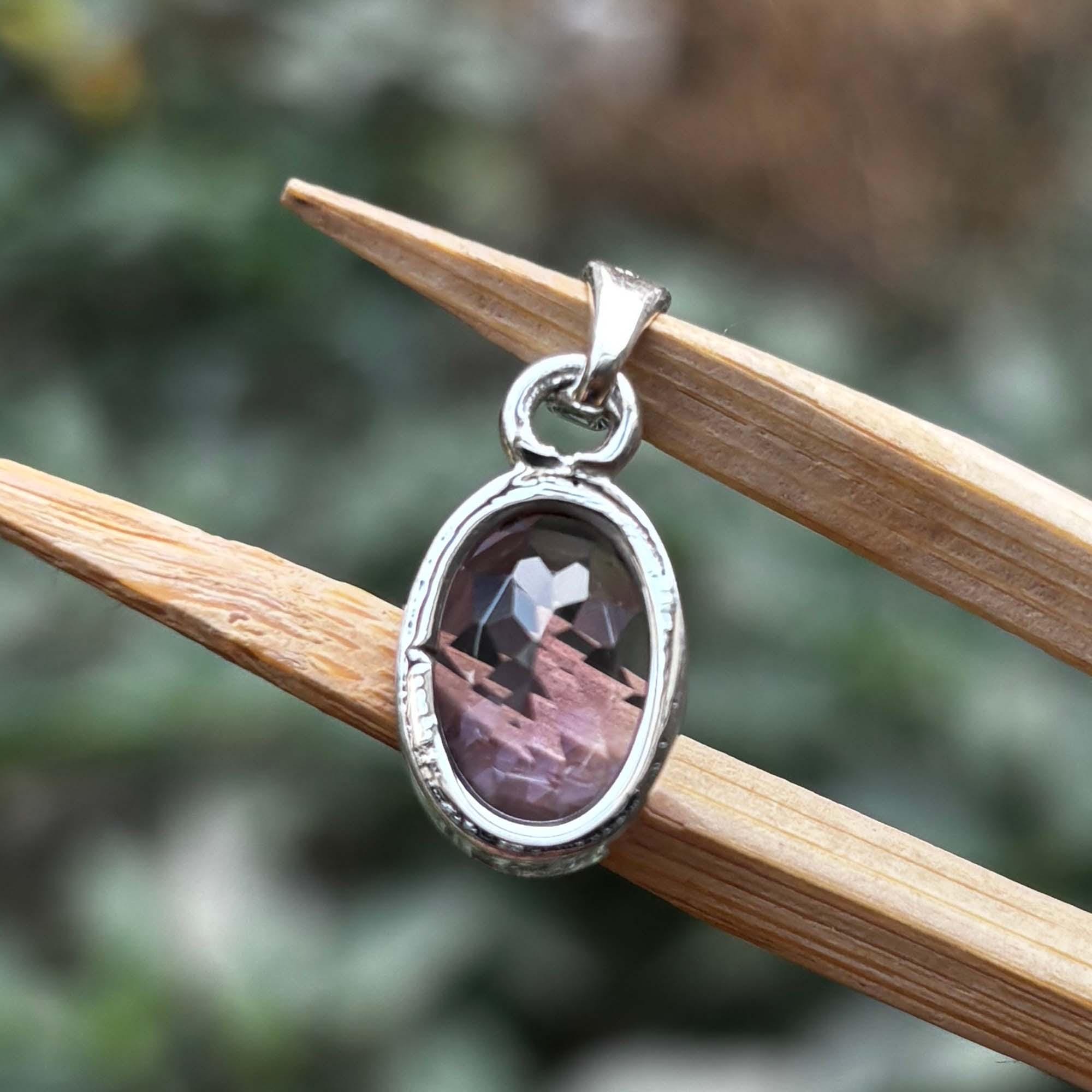 Silver pendant with a purple stone on a wooden stick against a blurred natural background