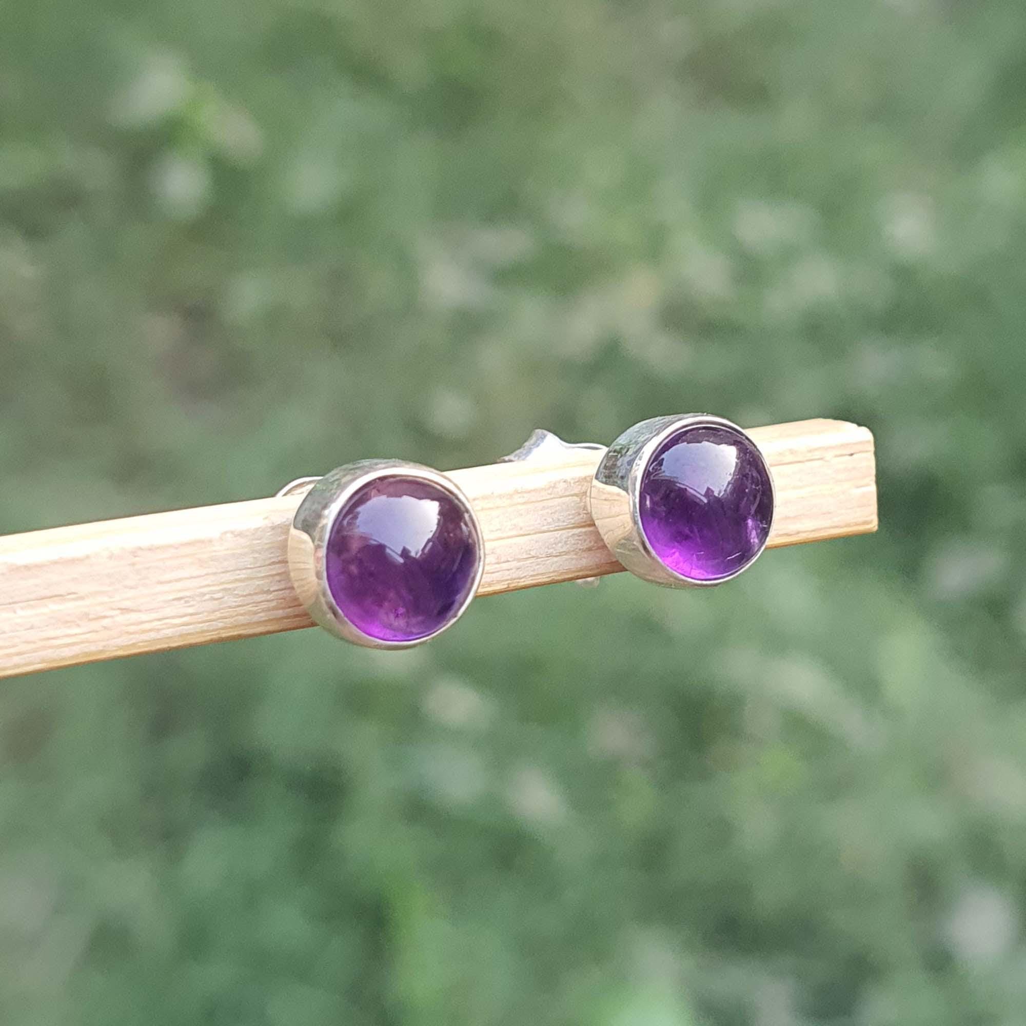 Amethyst stud earrings on a wooden stick with a blurred green background