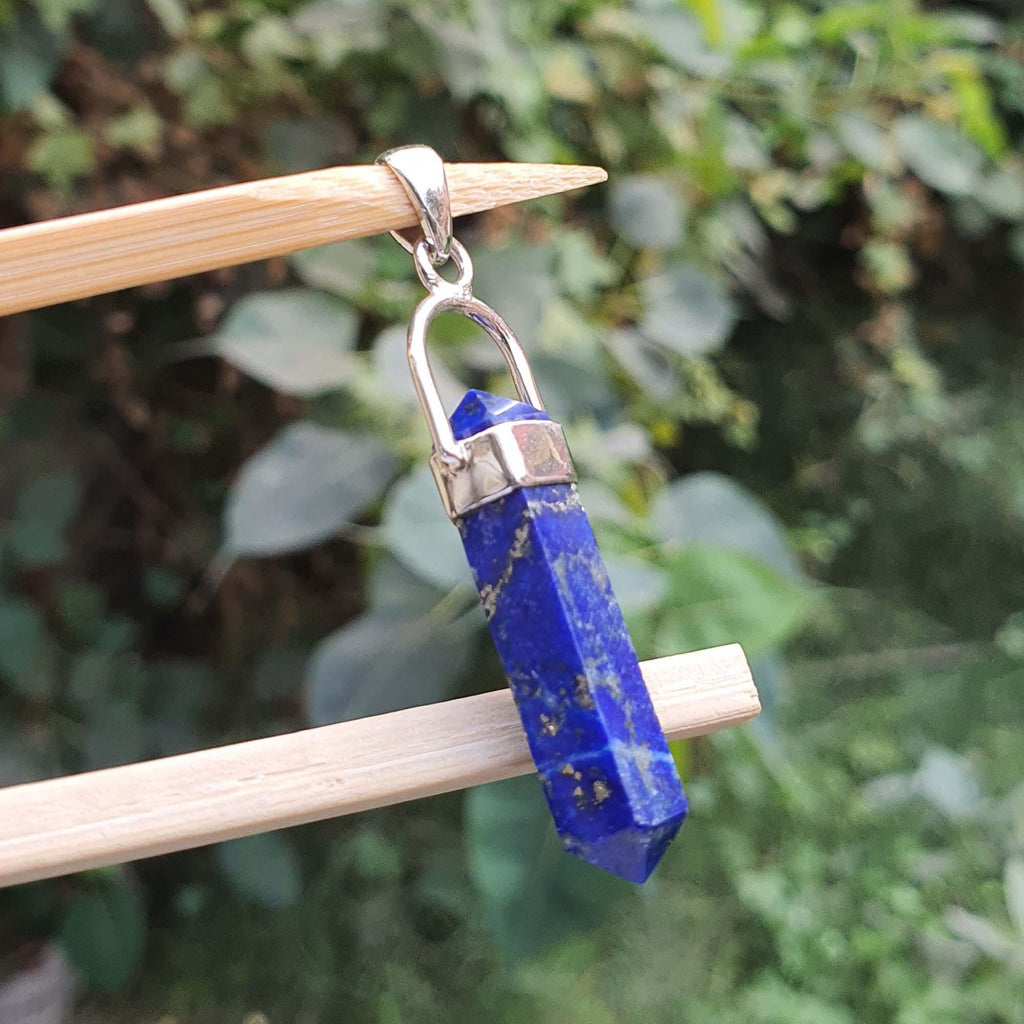 Blue crystal pendant on a wooden stick with a blurred green leafy background