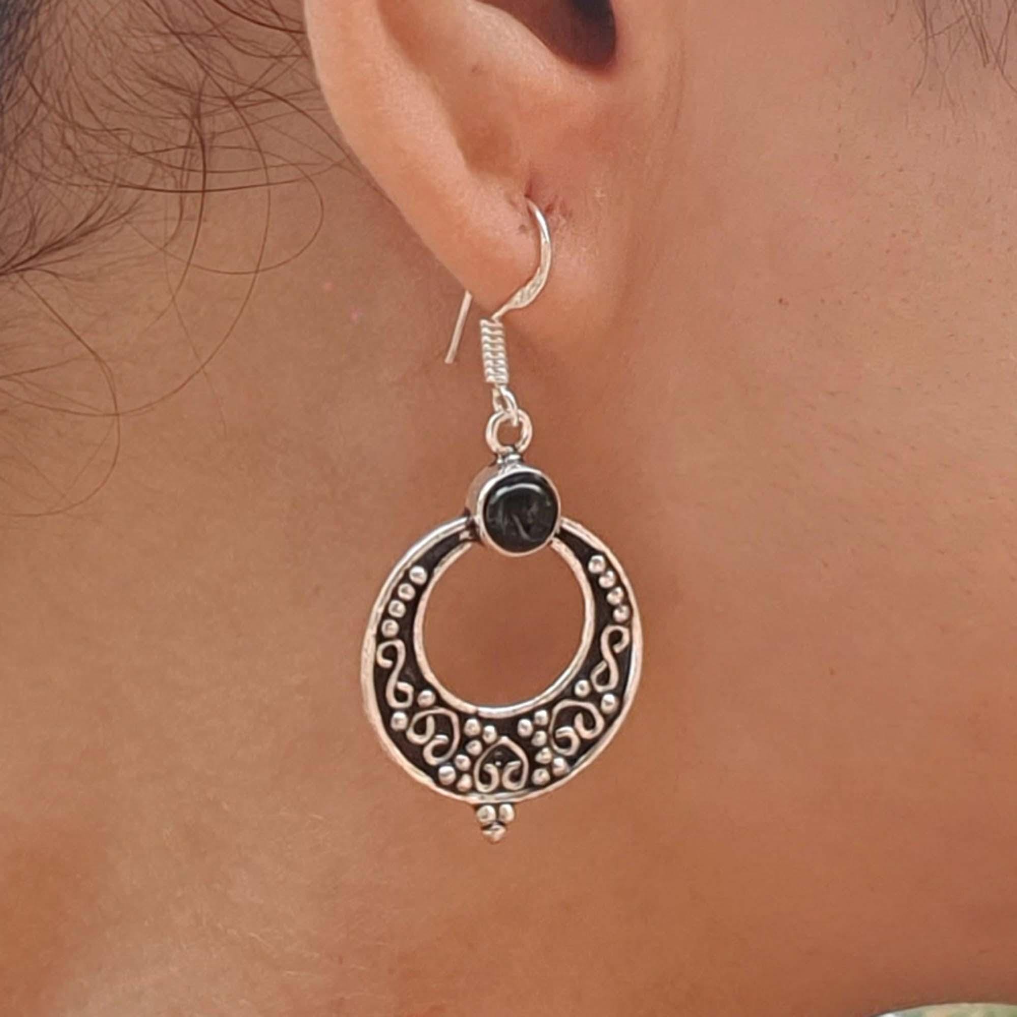 Silver hoop earring with black gemstone worn by a person