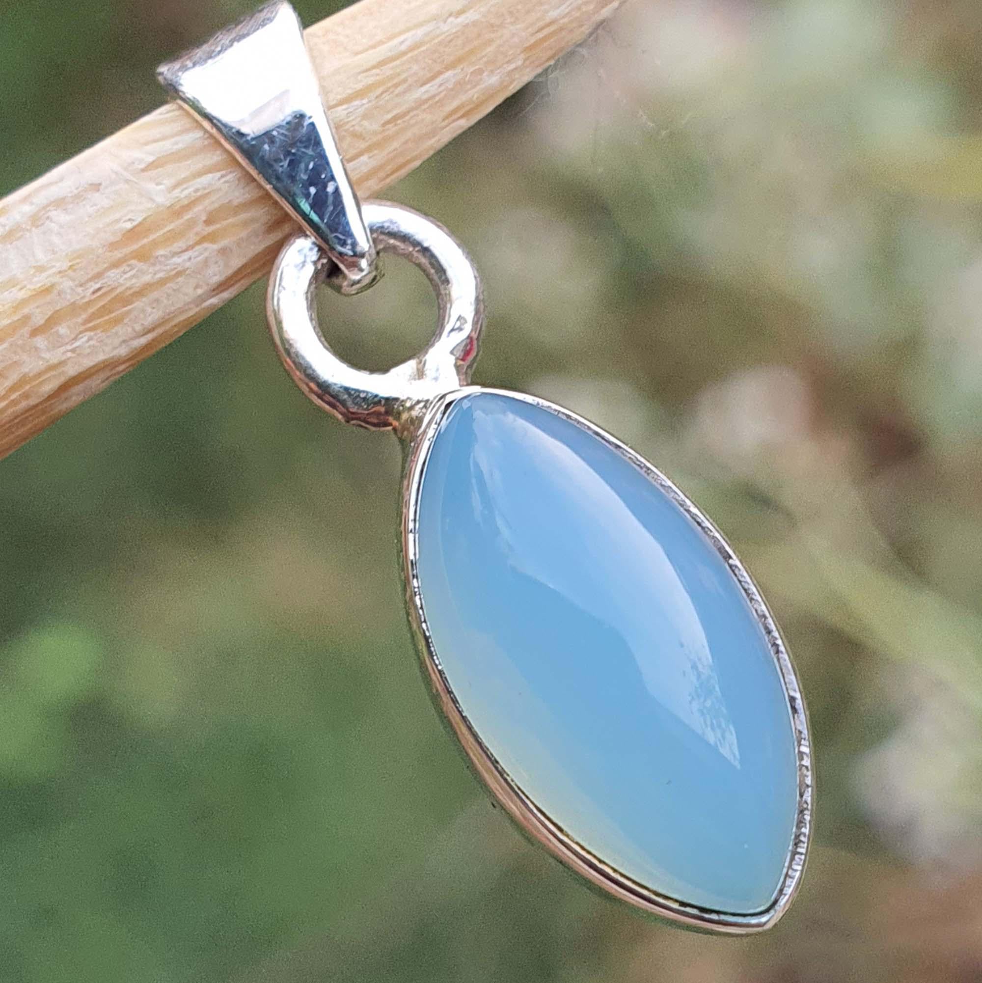 Teardrop-shaped blue stone pendant on a silver chain against a blurred natural background