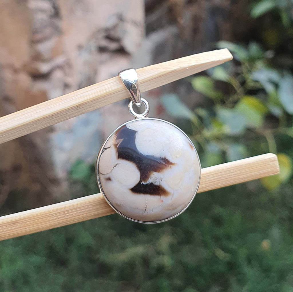 Round pendant with a brown and beige pattern on a wooden stick against a natural background