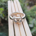 Silver ring with a unique design on a wooden surface with a blurred green background