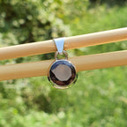 Round pendant with a black stone and gold rim on a wooden stick against a green blurred background
