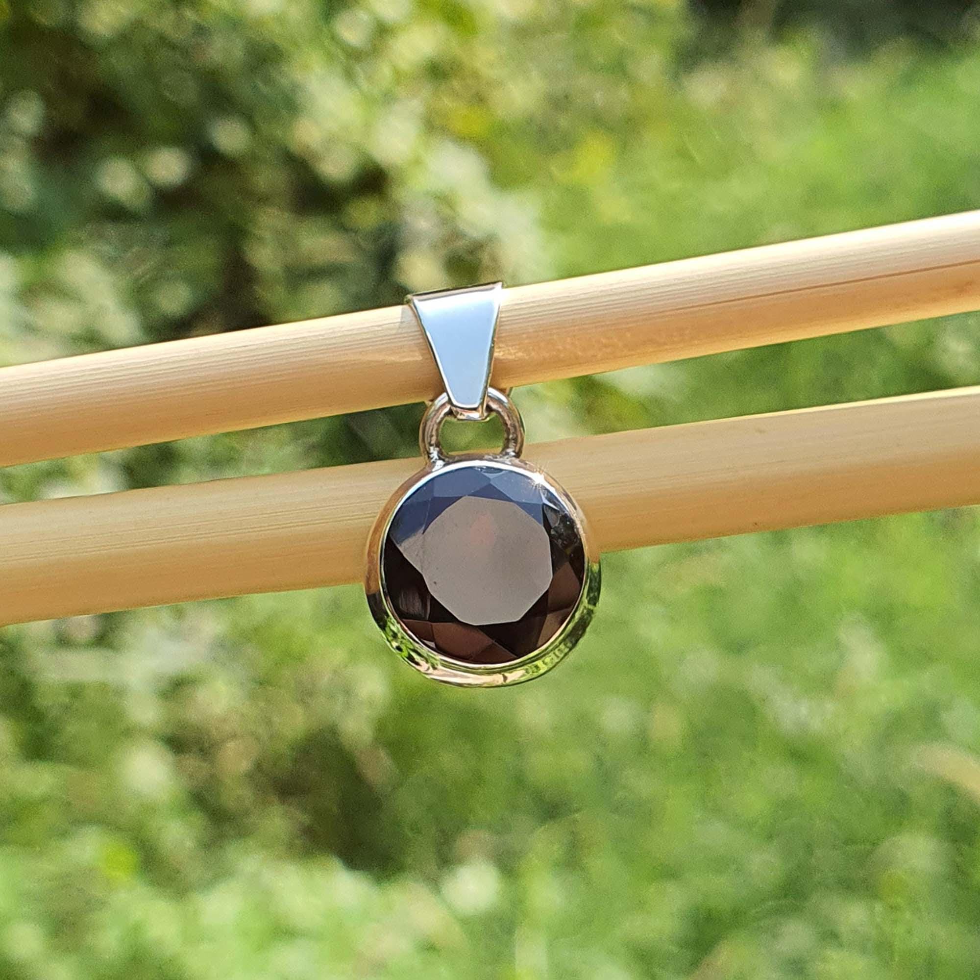 Round pendant with a black stone and gold rim on a wooden stick against a green blurred background