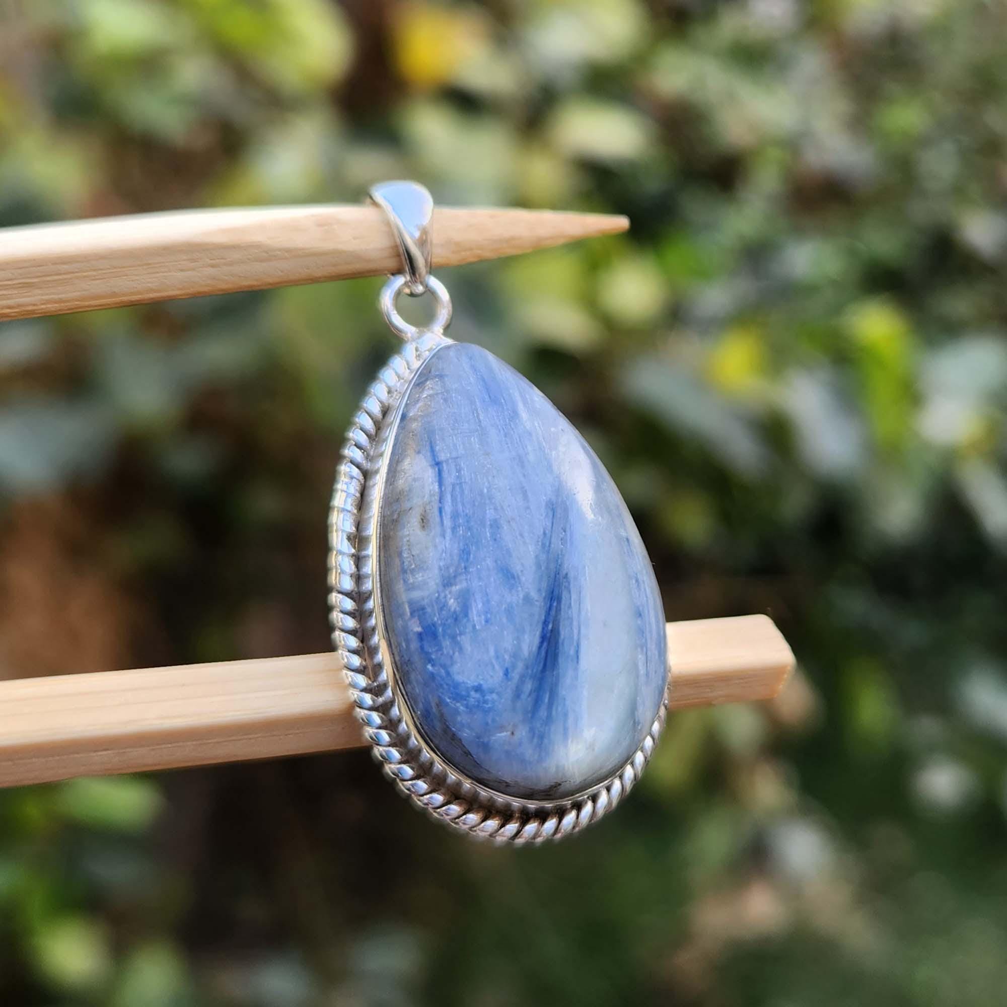 Blue teardrop pendant on a wooden stick with a blurred green background