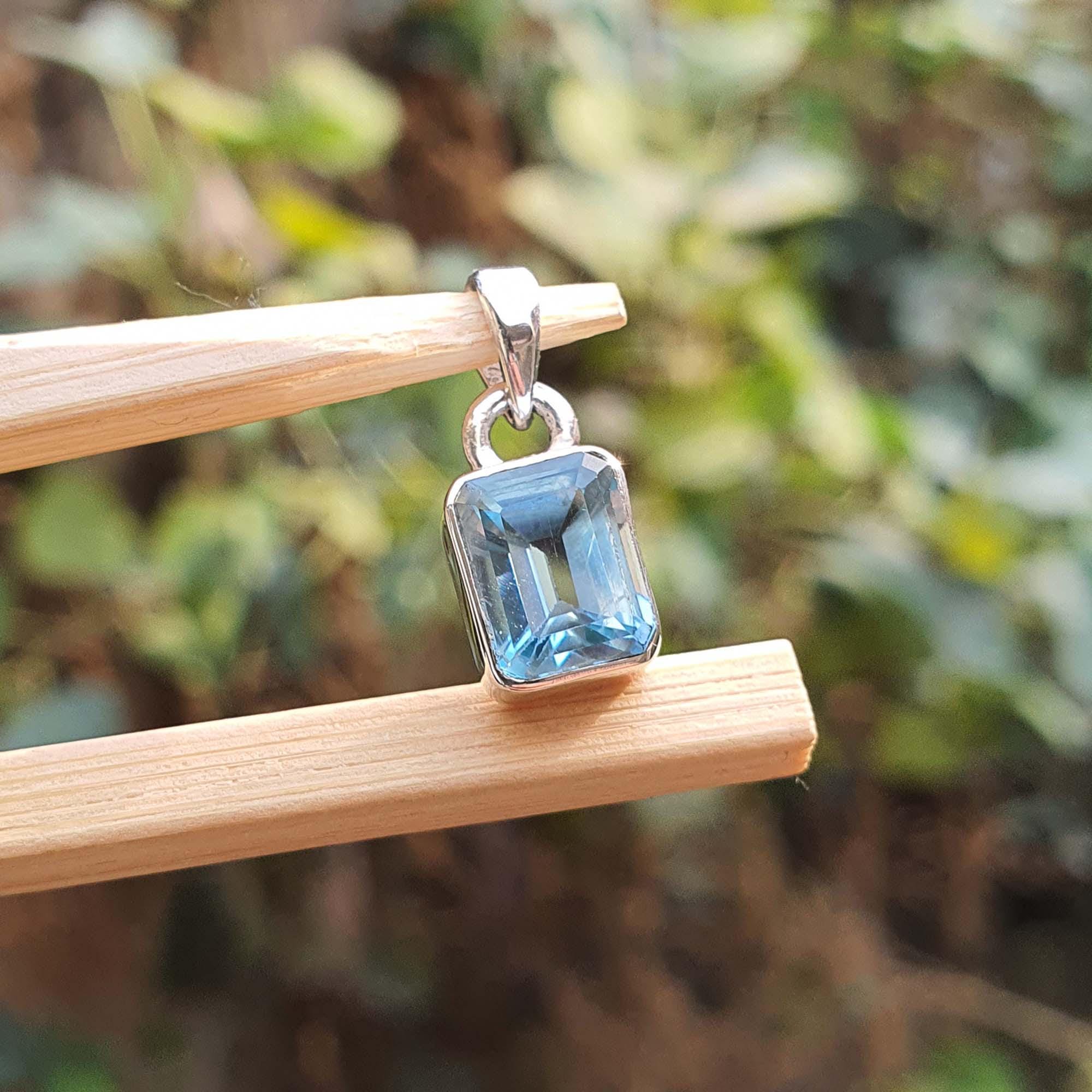 Blue gemstone pendant on a wooden stick with a blurred green background