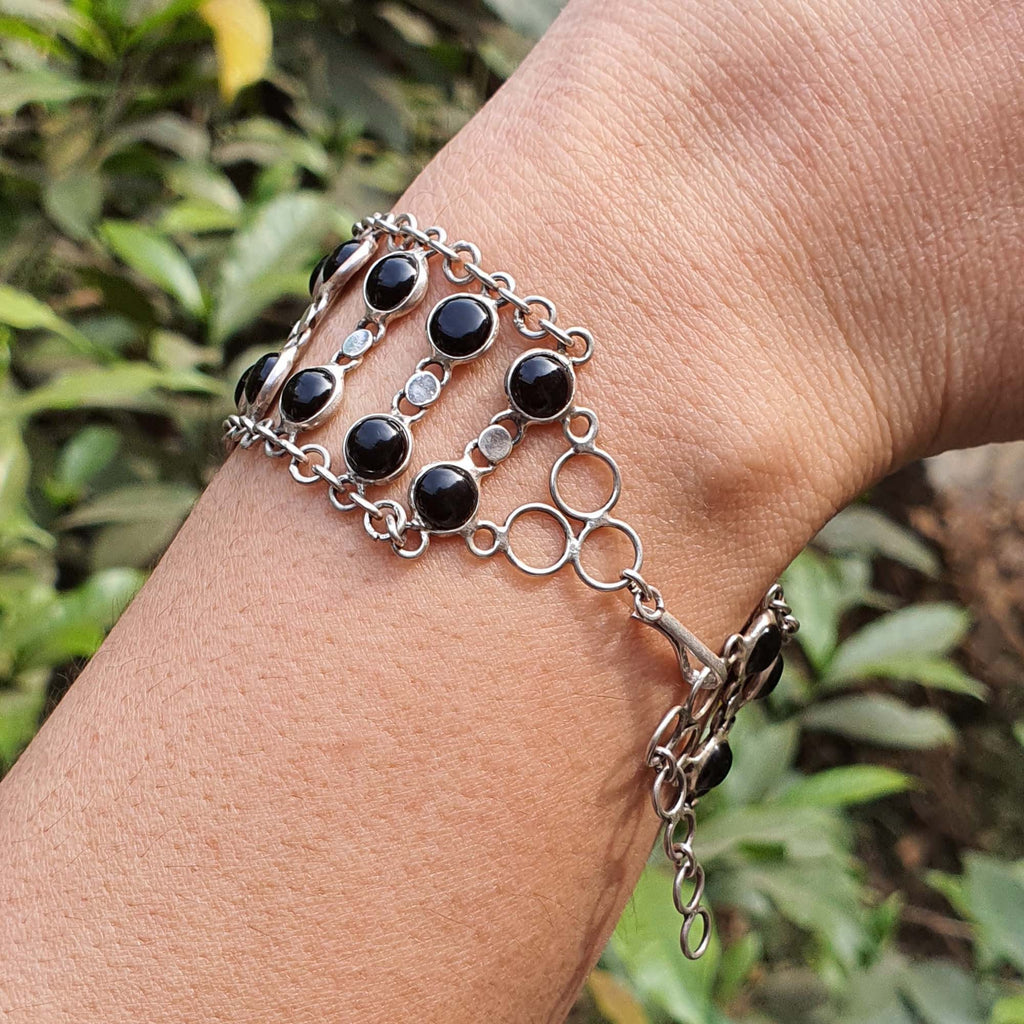 Silver bracelet with black stones on a wrist against a natural background