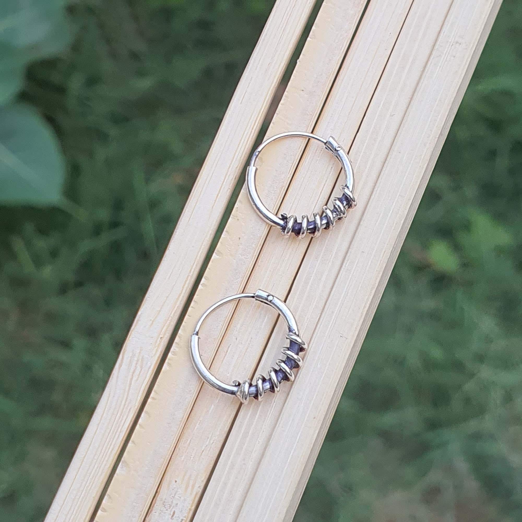 Pair of silver hoop earrings on a wooden surface with a natural background