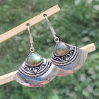 Silver earrings with green gemstones on a wooden stick against a blurred green background