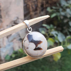 Round stone pendant on a silver chain, hanging on a wooden stick with a natural background.