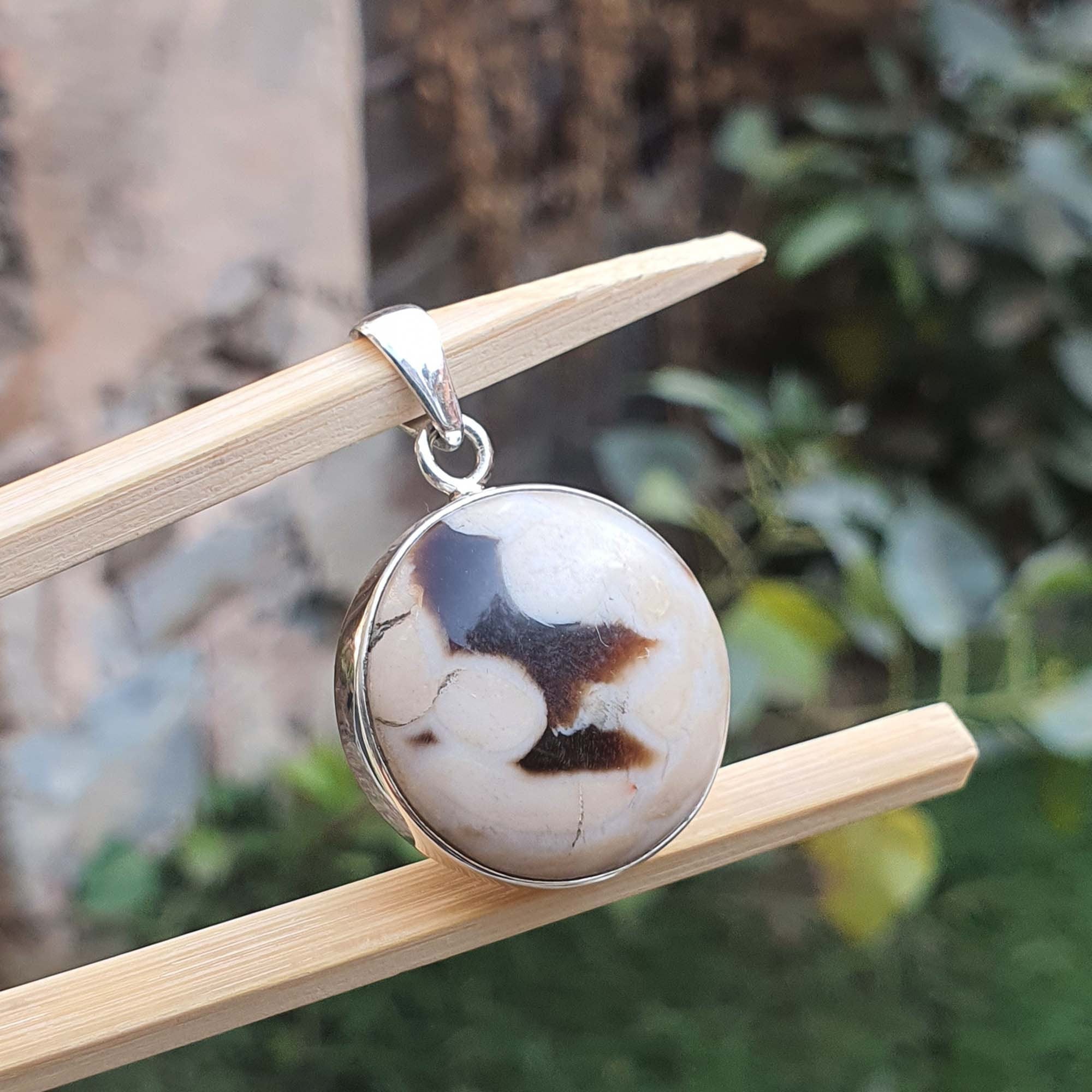 Round stone pendant on a silver chain, hanging on a wooden stick with a natural background.