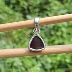 Silver pendant with a red stone on a wooden stick against a green background