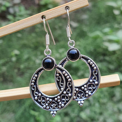 Silver hoop earrings with black stones on a wooden stick against a blurred green background