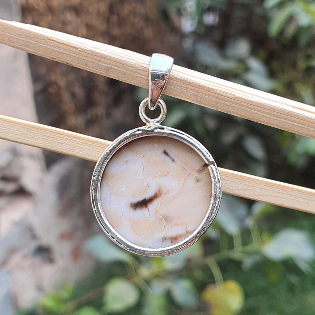 Silver pendant with a natural stone design hanging on a branch with a blurred natural background
