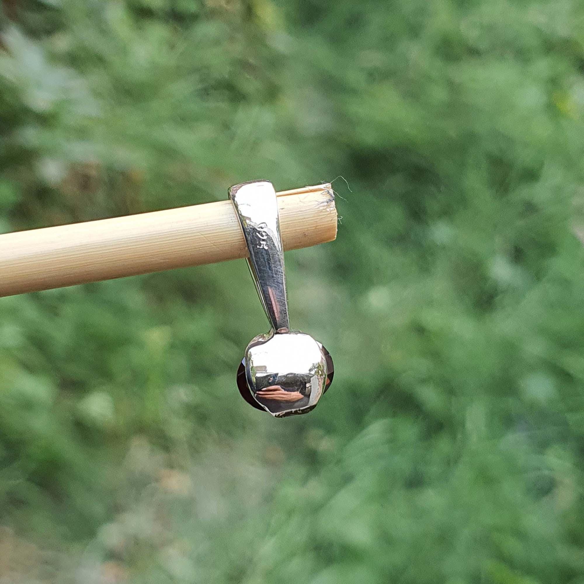 Silver pendant on a stick with a blurred green background