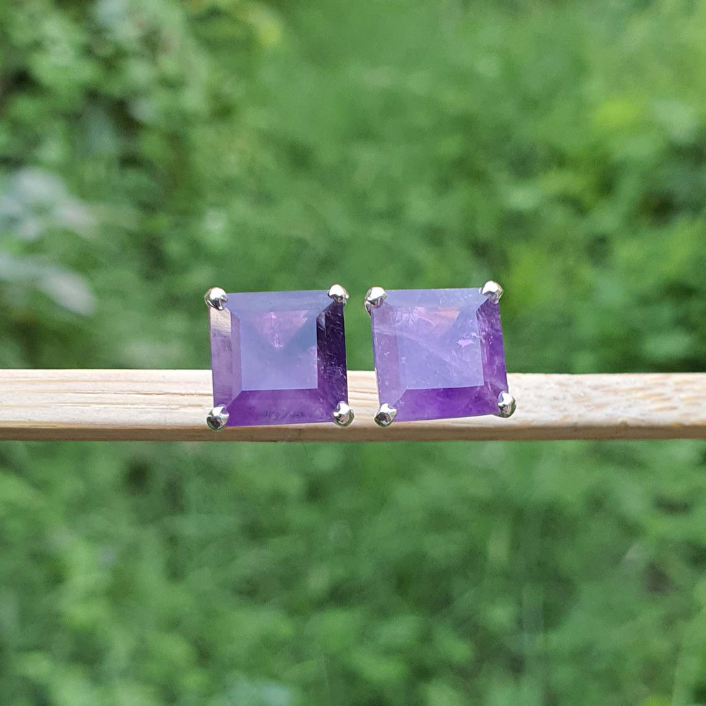 Pair of purple square gemstone earrings on a wooden stick with a green blurred background