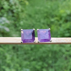 Pair of purple square gemstone earrings on a wooden stick with a green blurred background