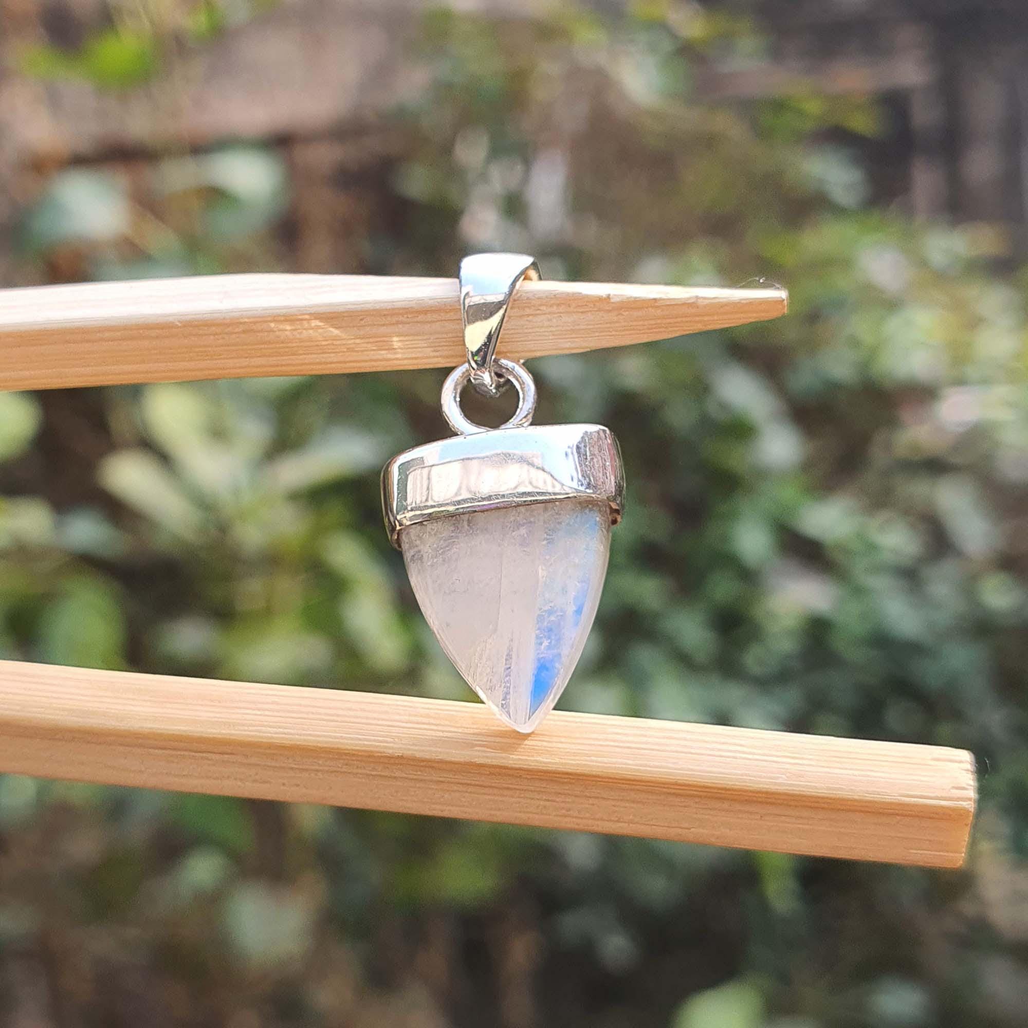 Silver pendant with a clear gemstone on a wooden stick against a blurred green background
