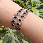 Silver bracelet with black beads on a wrist against a green leafy background