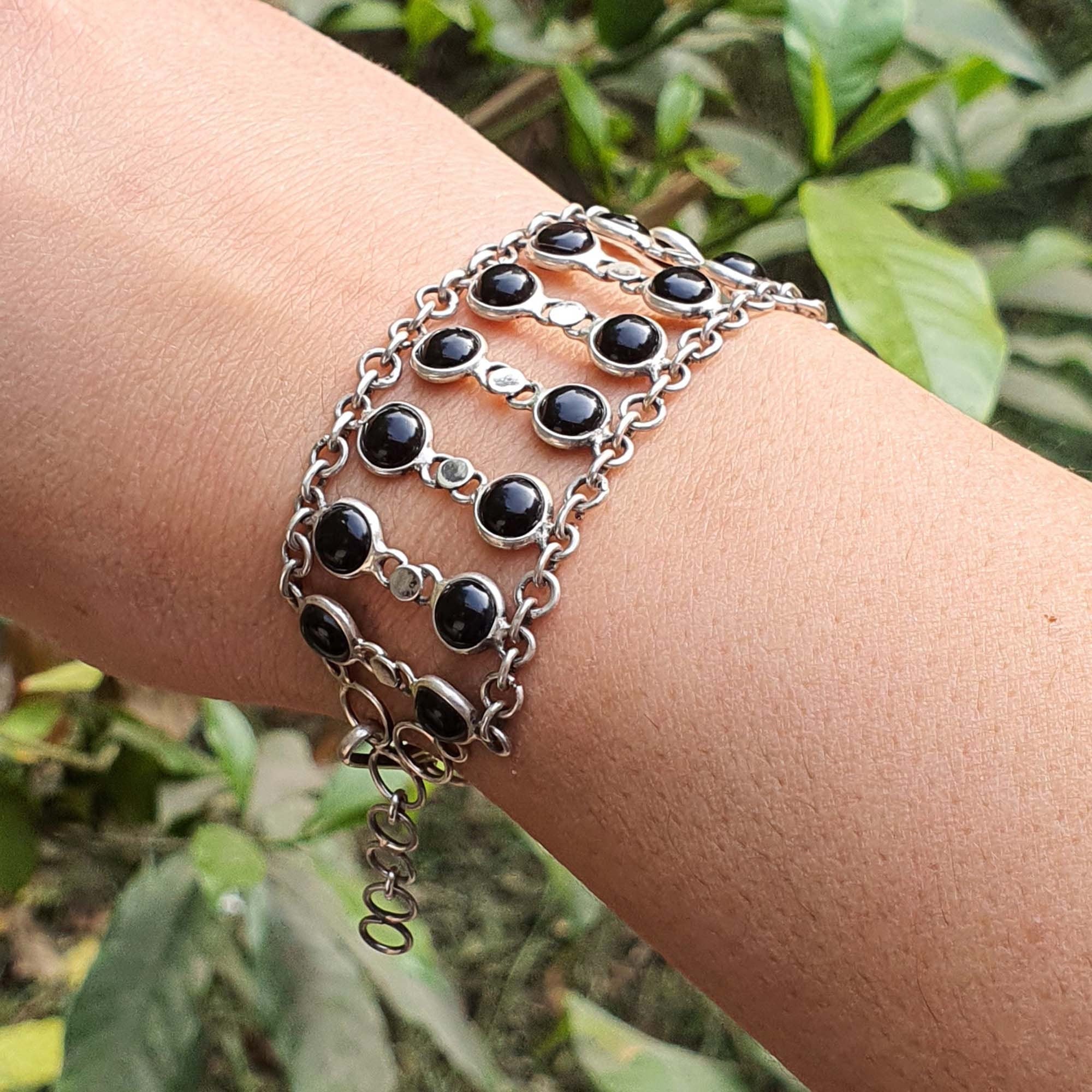 Silver bracelet with black beads on a wrist against a green leafy background