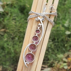 Silver necklace with pink gemstones on a wooden stick against a natural background