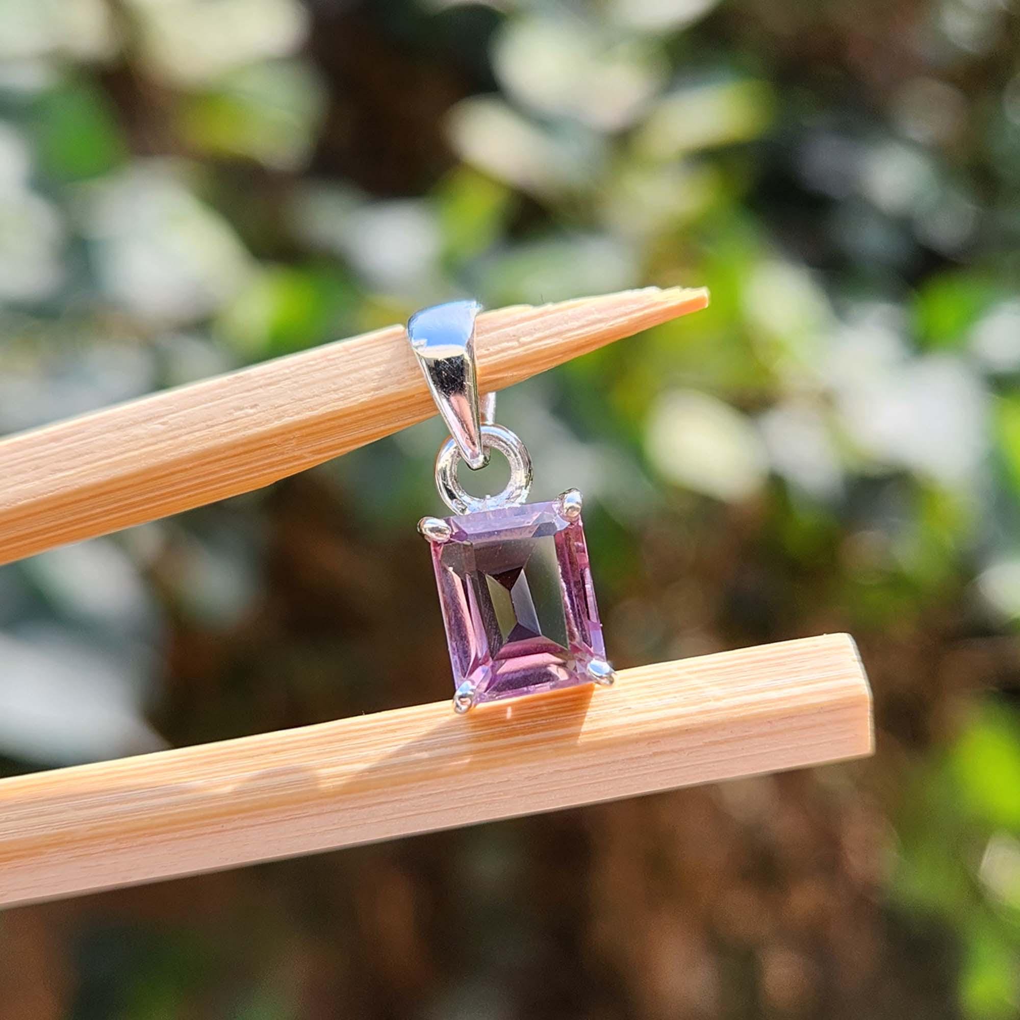 Purple gemstone pendant on a wooden stick with a blurred green background