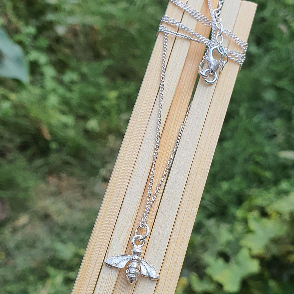 Silver bee pendant necklace on a wooden stick with a natural green background