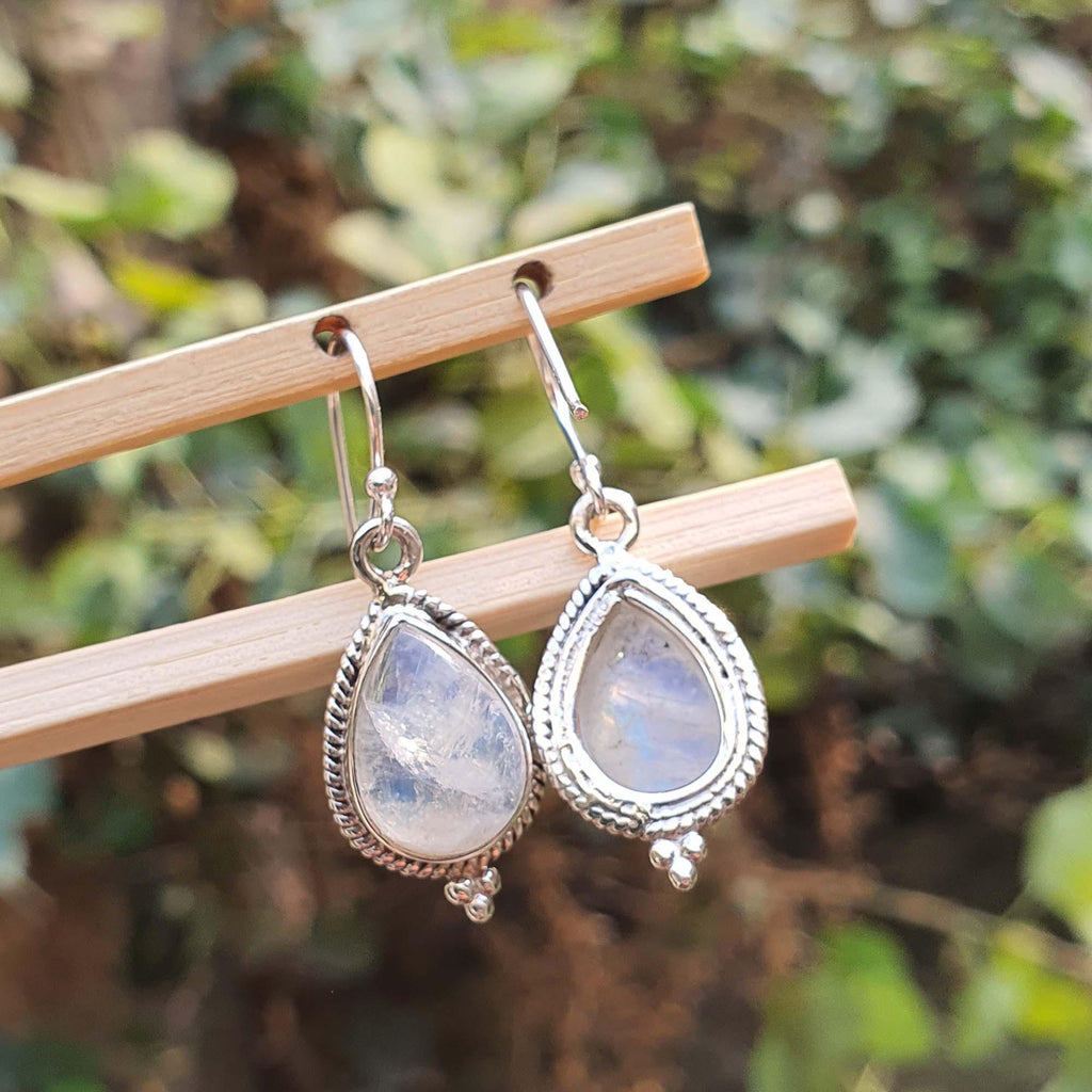 Teardrop-shaped earrings with a silver frame on a wooden stick against a blurred green background