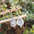 Teardrop-shaped earrings with a silver frame on a wooden stick against a blurred green background