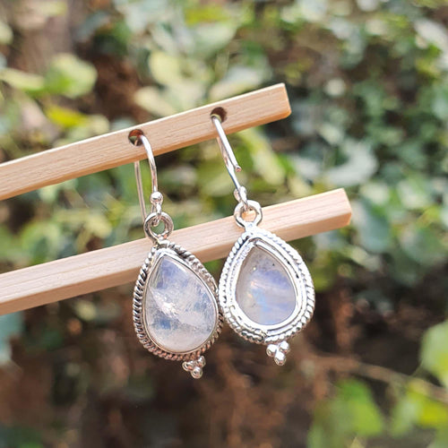 Teardrop-shaped earrings with a silver frame on a wooden stick against a blurred green background