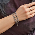 Person wearing a silver bracelet with black beads on a dark background