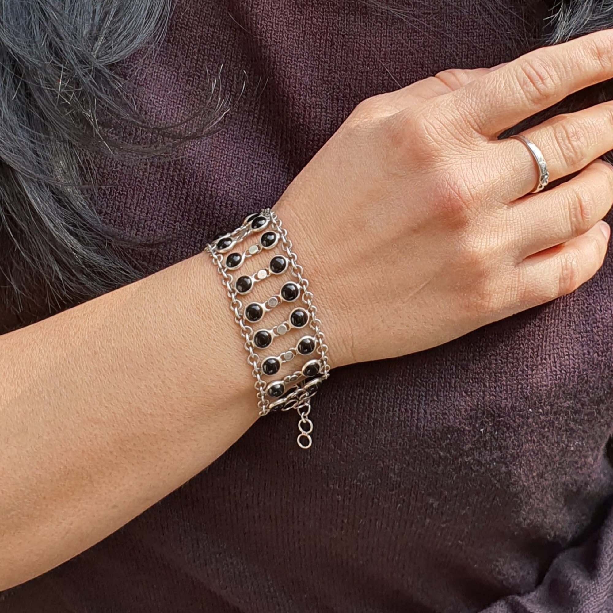 Person wearing a silver bracelet with black beads on a dark background