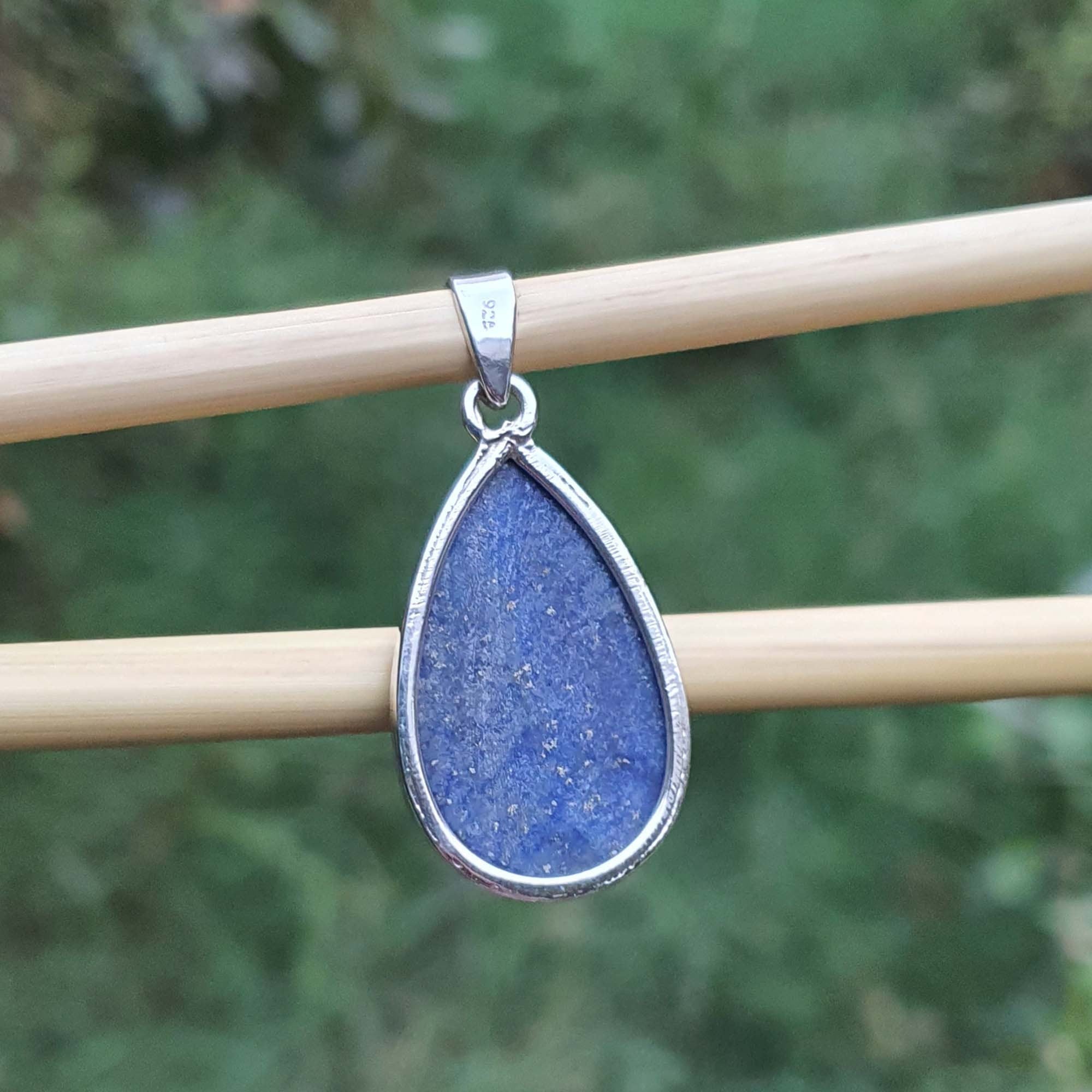 Blue teardrop pendant with silver frame on a wooden stick against a blurred green background