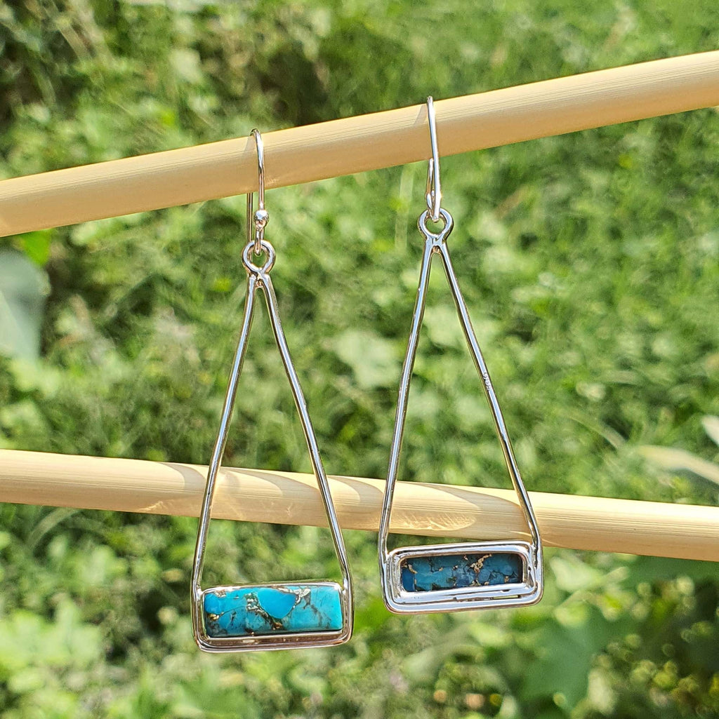 Silver earrings with turquoise stones on a wooden stick against a green grass background