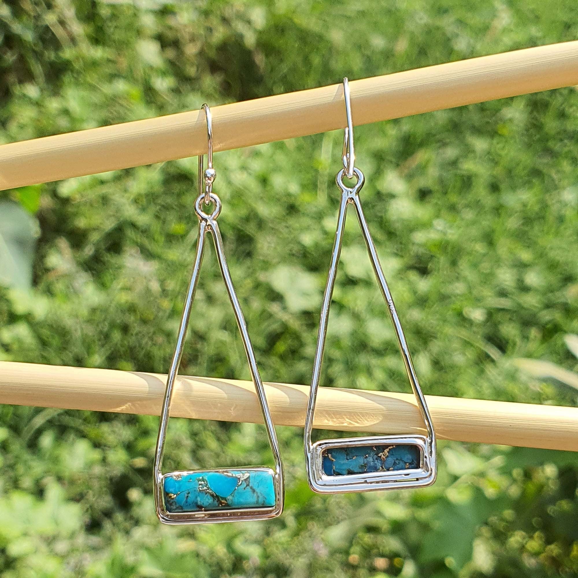 Silver earrings with turquoise stones on a wooden stick against a green grass background