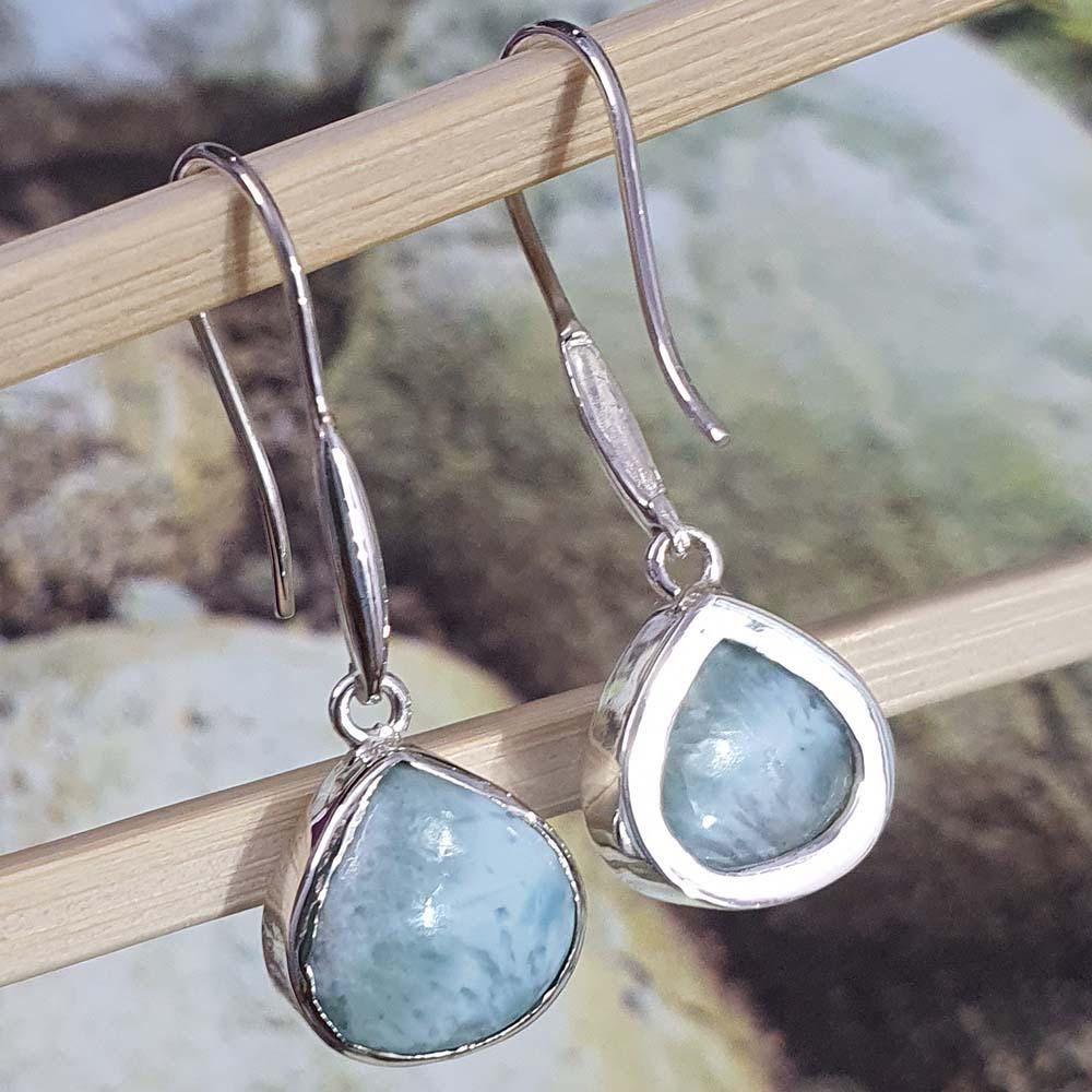 Silver earrings with blue stones hanging on a wooden stick.