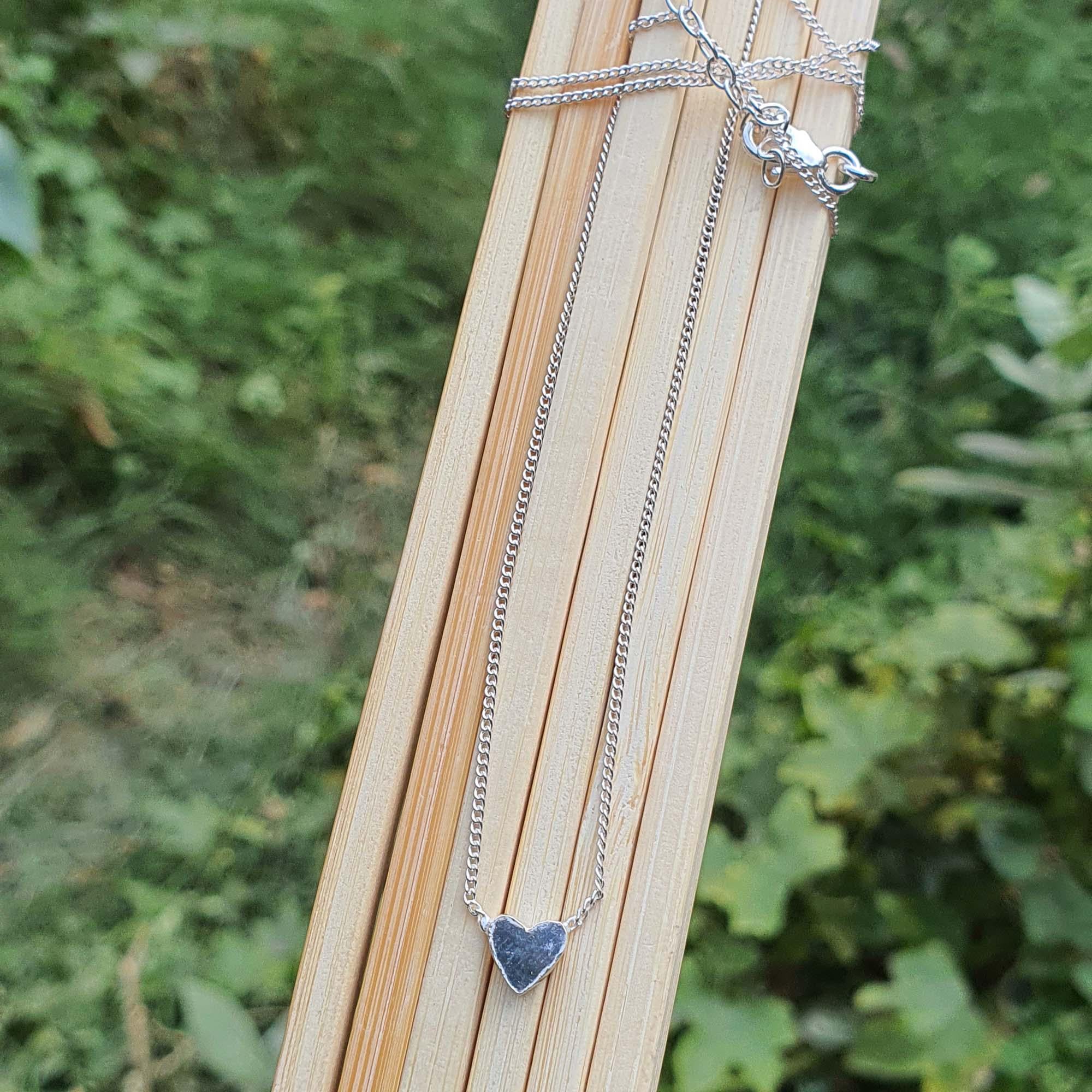 Silver necklace with a heart pendant on a wooden stick against a green leafy background