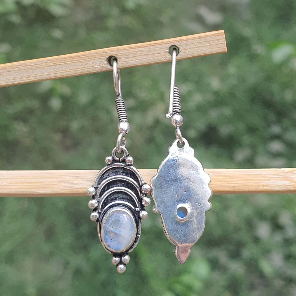 Pair of silver earrings with gemstones on a wooden stick against a blurred green background