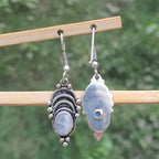 Pair of silver earrings with gemstones on a wooden stick against a blurred green background