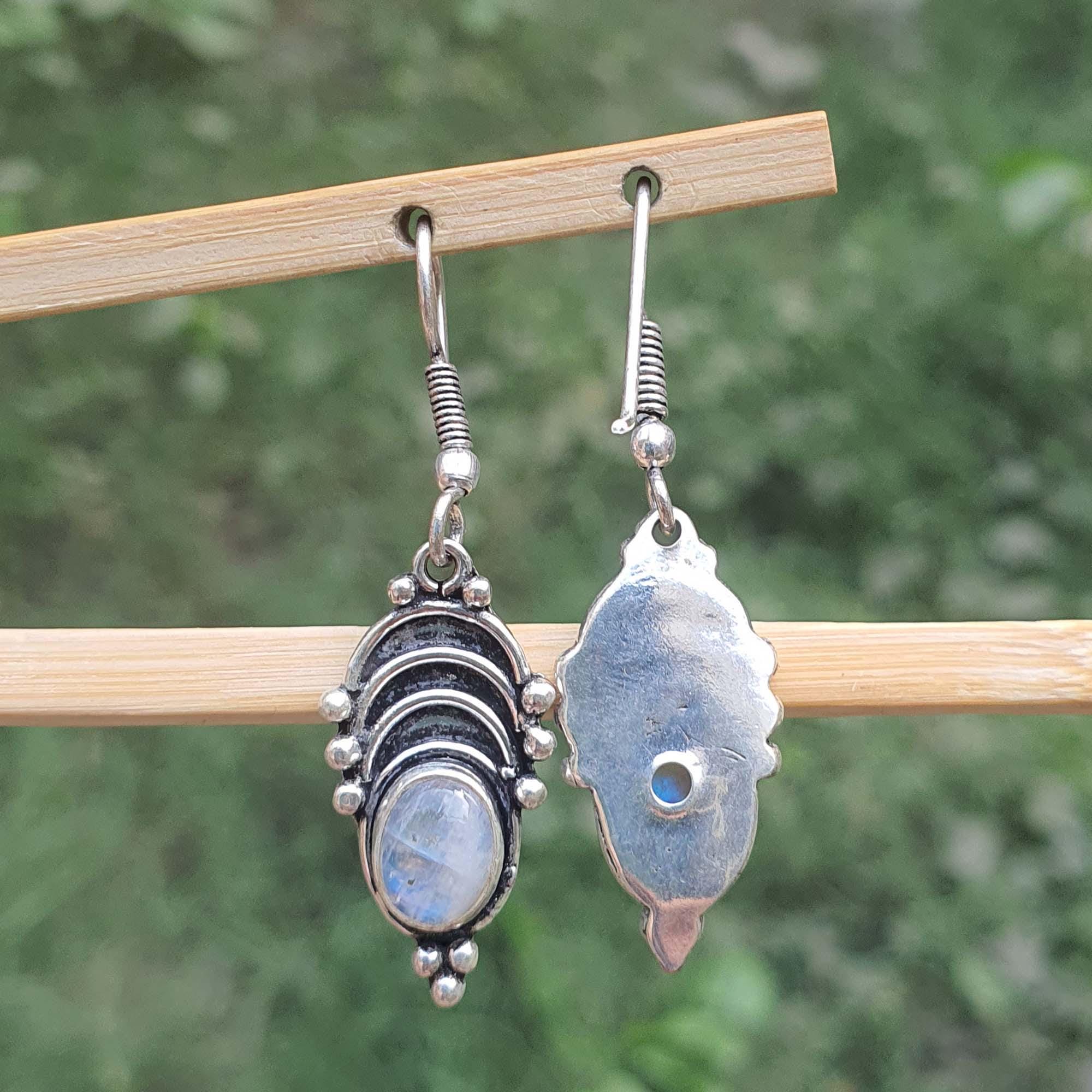 Pair of silver earrings with gemstones on a wooden stick against a blurred green background